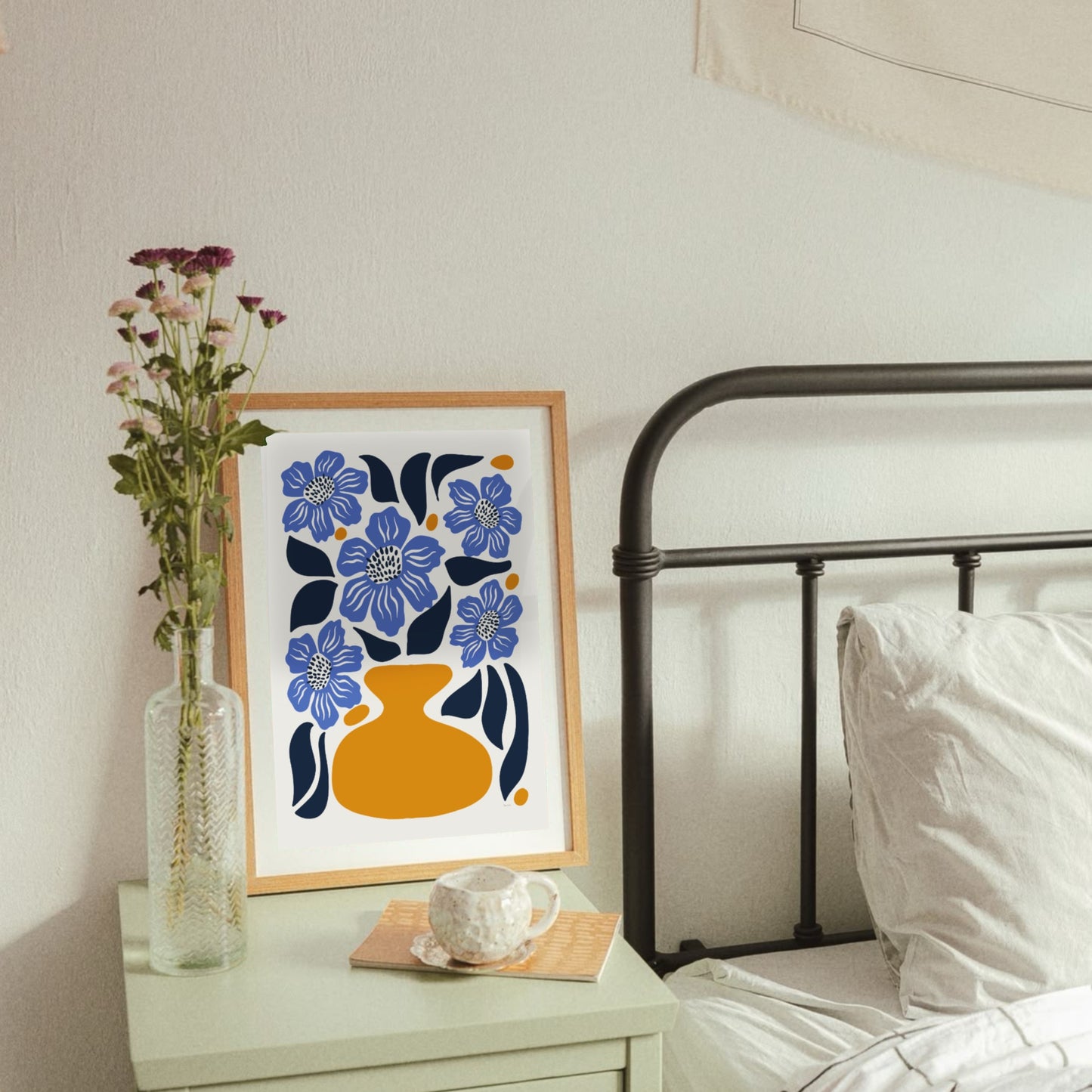 Vallmopostern med blå blommor och orange vas inramad i en ljus träram hängandes på en ljus vägg