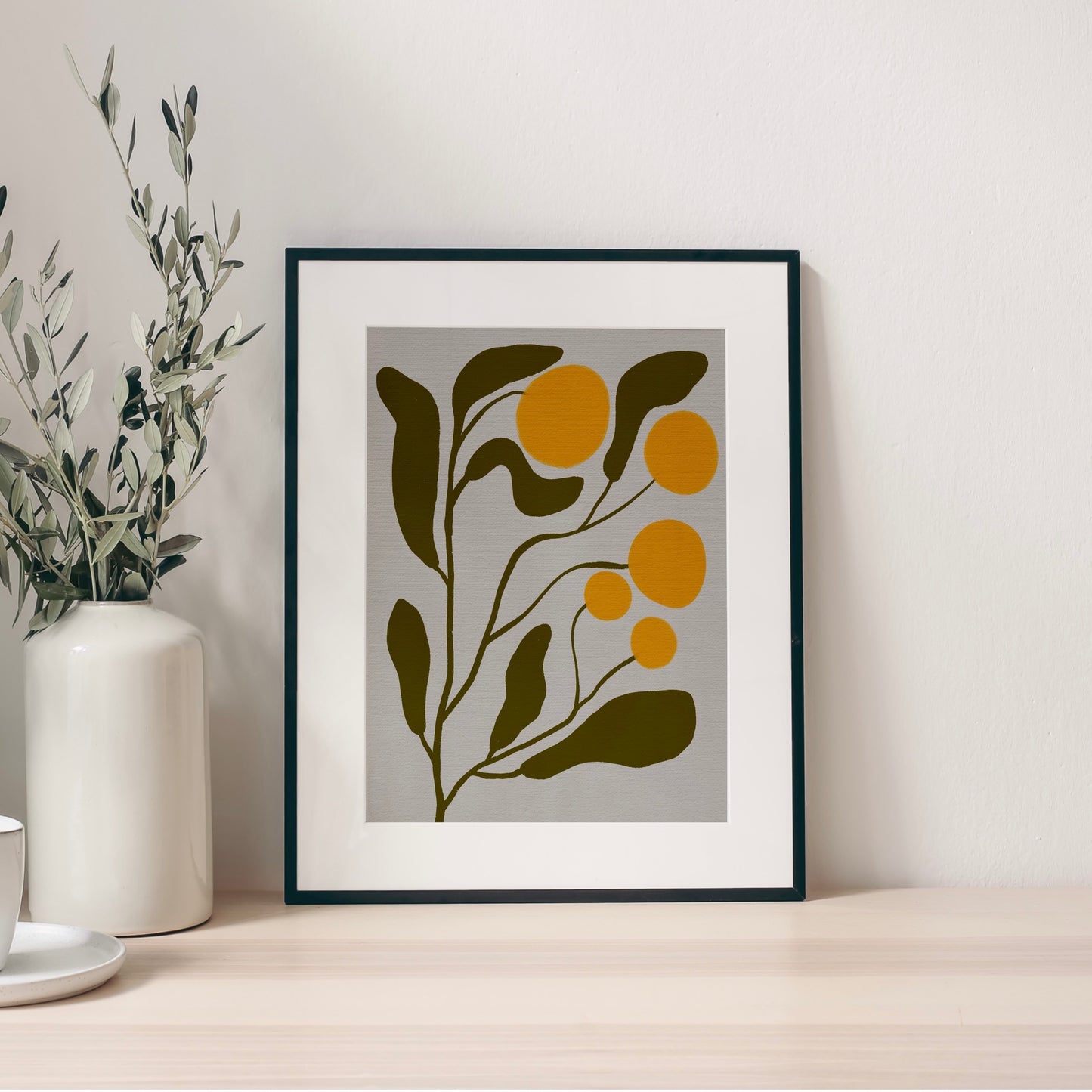 En inramad abstrakt mimosa-poster lutandes på en bänk i ett ljust och modernt kök.