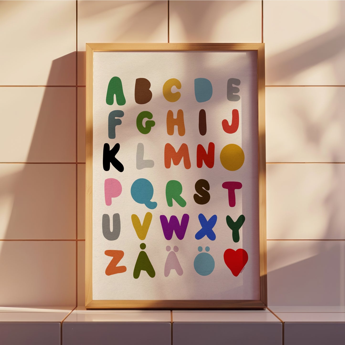 Alfabetspostern inramad i en ljus träram som står på en hylla i ett barnrum med mjukt solljus och skuggspel. Visar en lekfull och modern inredningsstil.