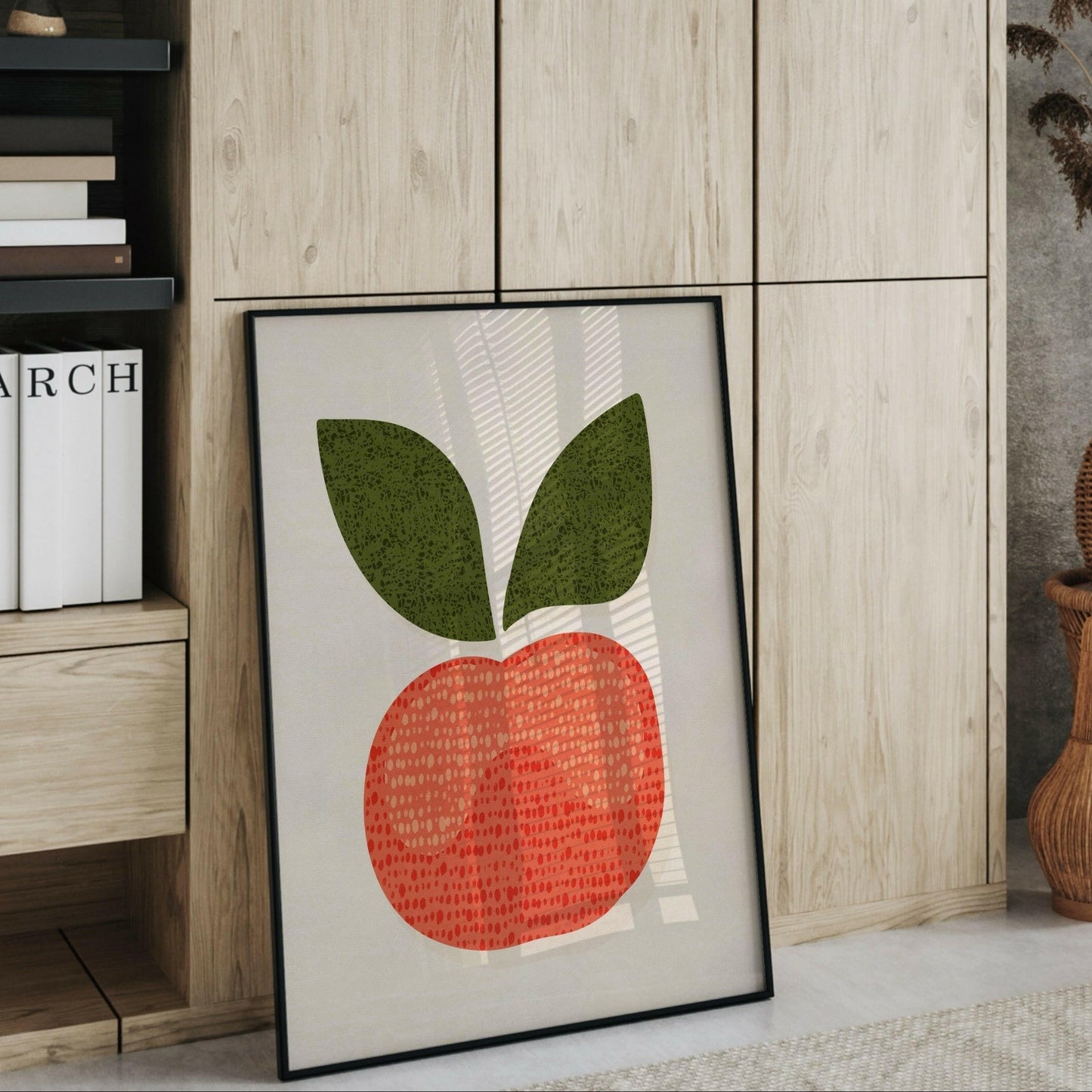 Äppel-postern i en svart ram som lutar mot en hylla med böcker