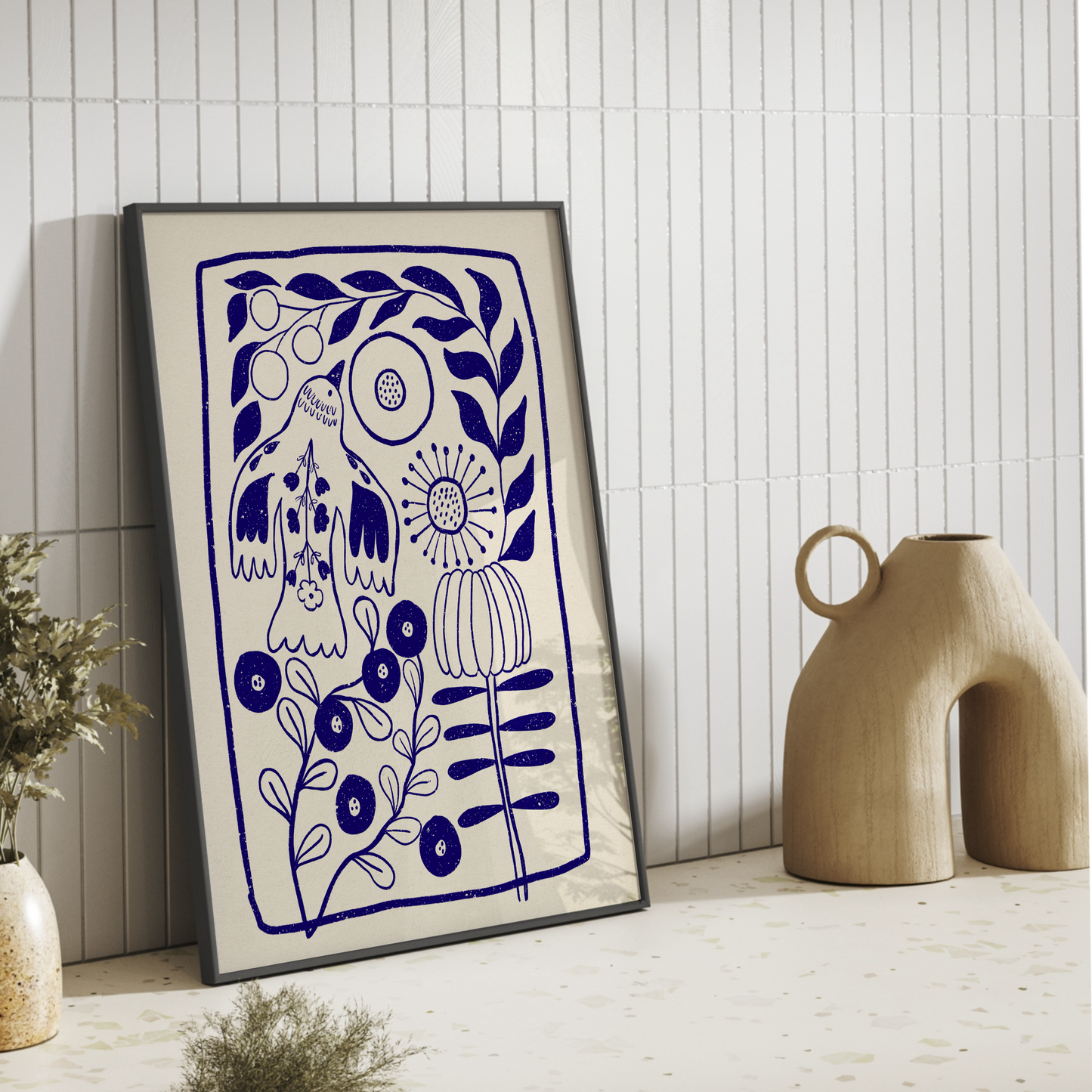 Modern blå poster lutad mot en beige kakelvägg i ett stilrent kök bredvid en skulptural keramikvas.