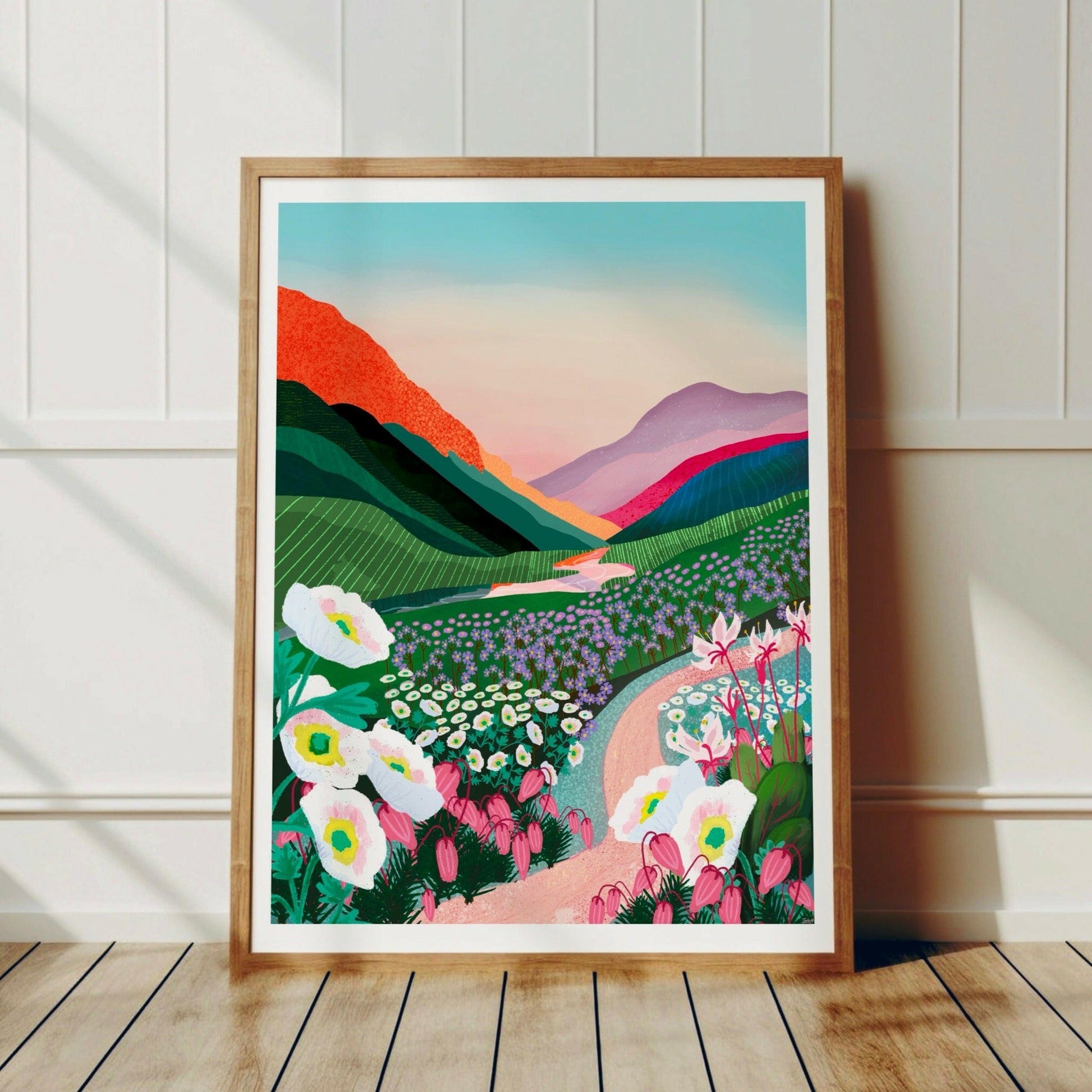 Kebnekaise-postern inramad i en ljus träram lutandes mot en vit trävägg i ett modernt vardagsrum med skandinavisk inredning. Visar hur motivet skapar en lugn och inspirerande känsla mot väggen.