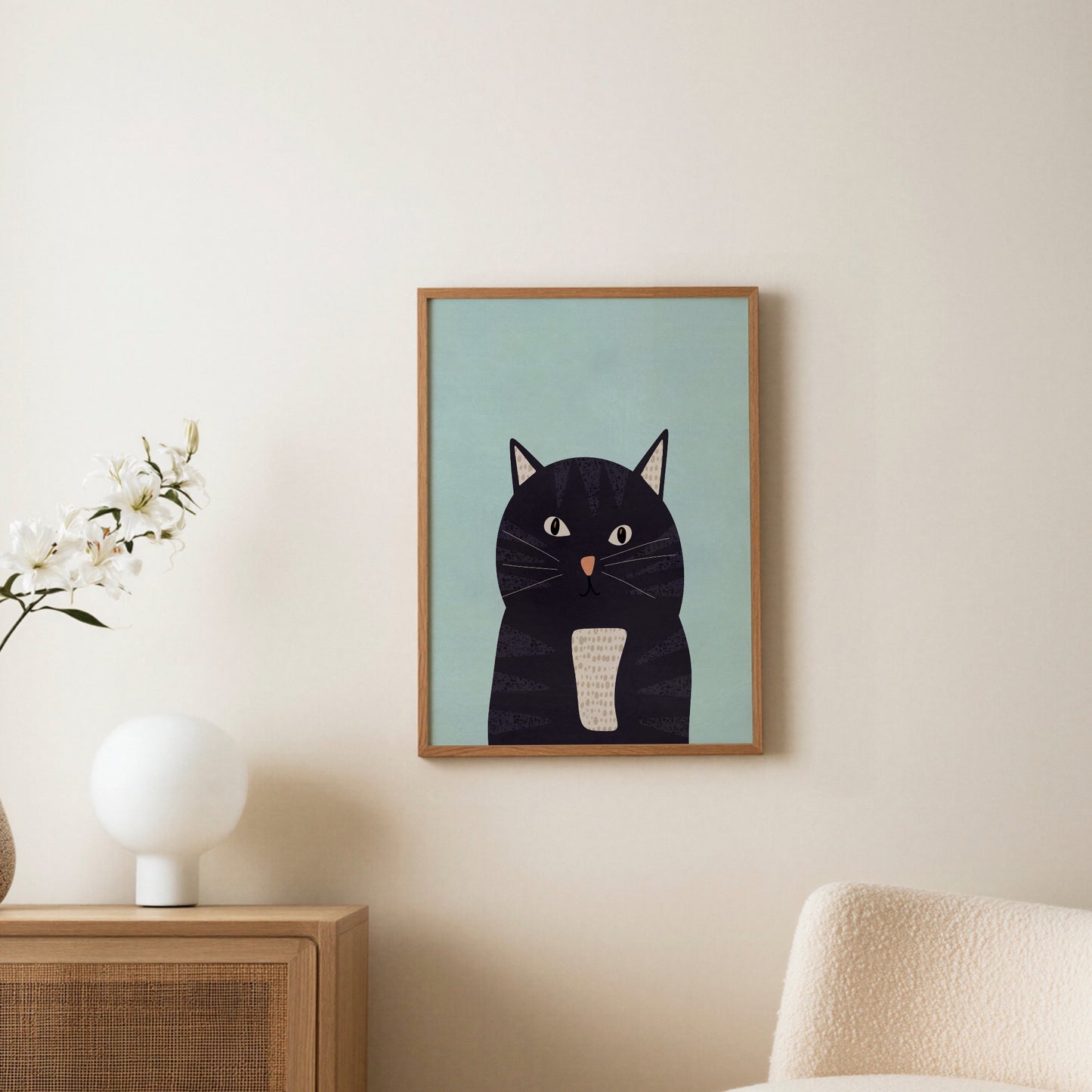 Kattposter i ljus träram uppsatt på vägg ovanför en byrå, med en bordslampa och en blomma i rummet