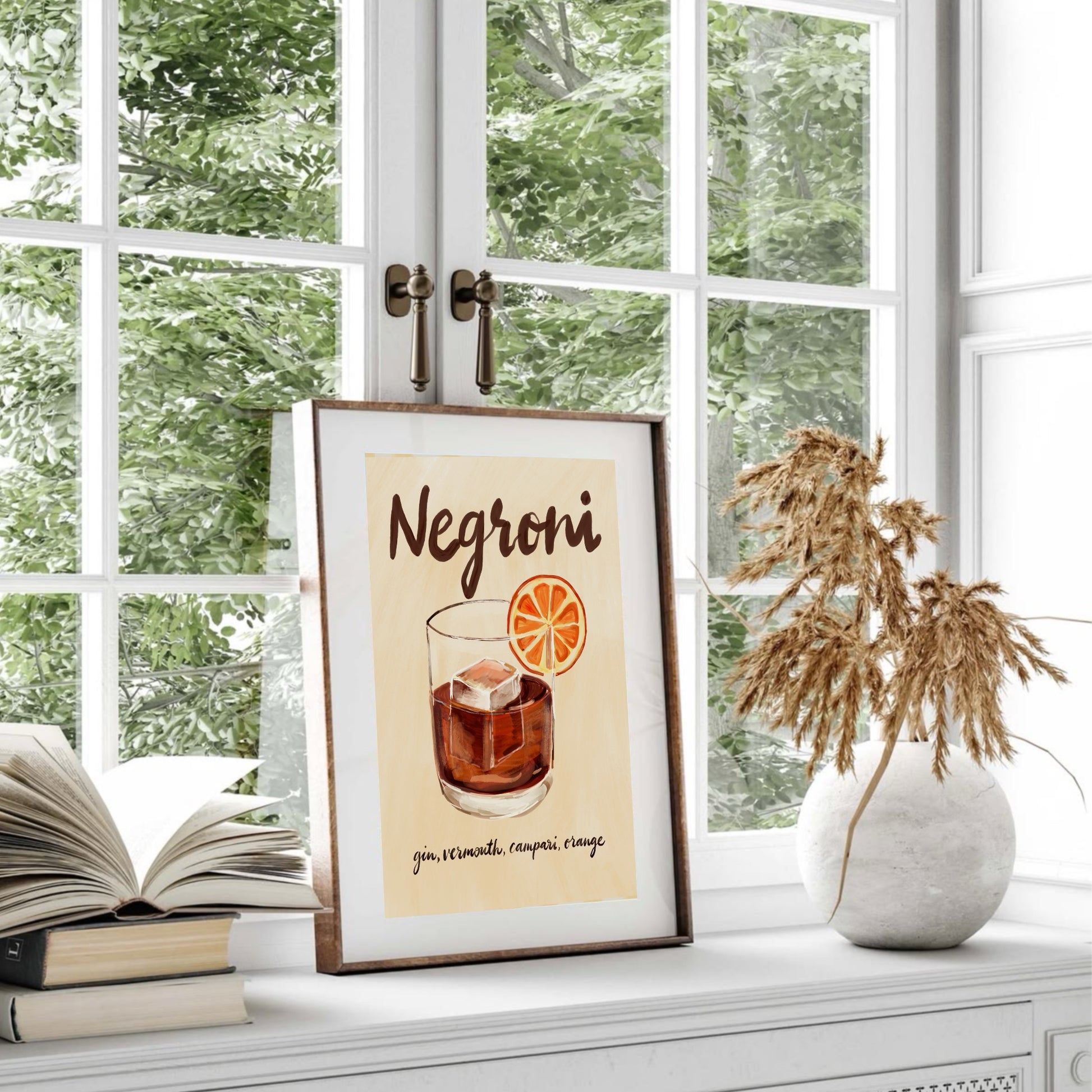 Negroni-poster i ram bredvid ett fönster med naturligt ljus och torkade blommor