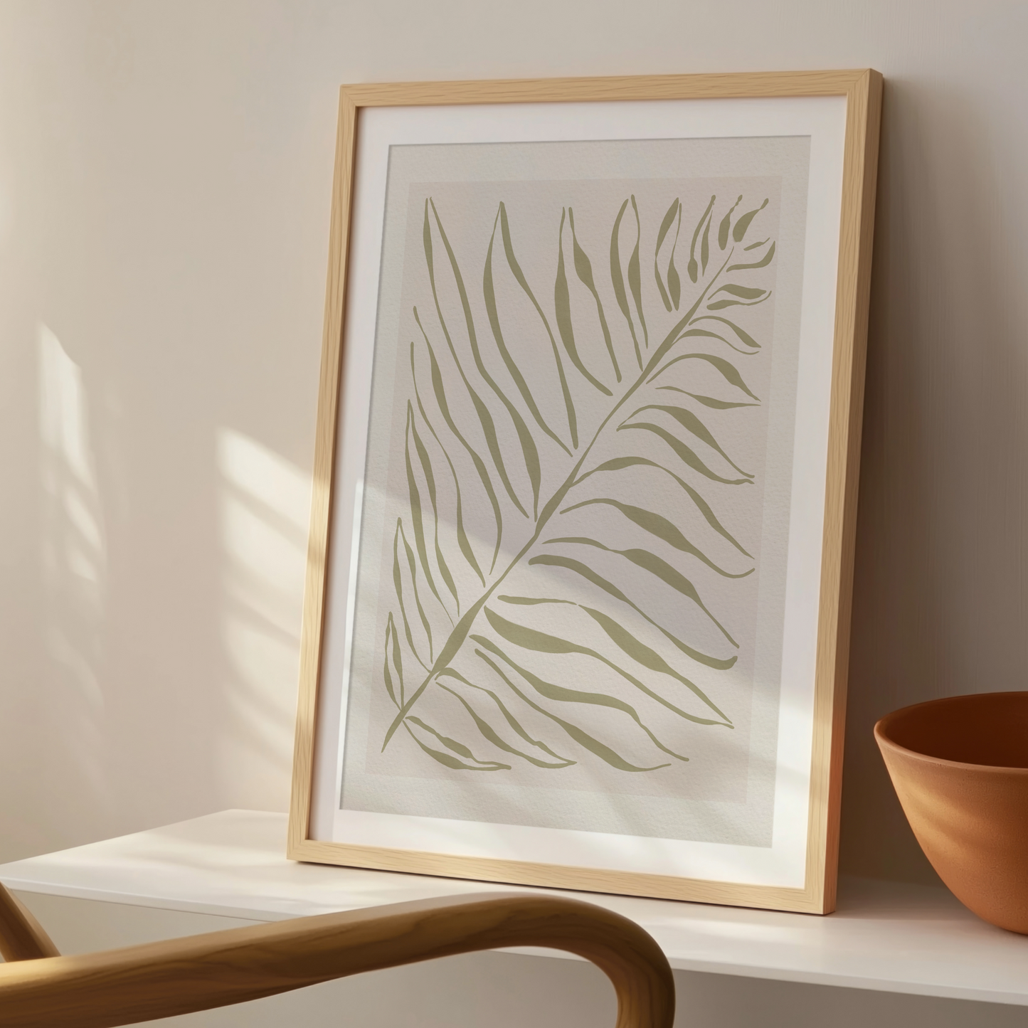 Akvarellposter med palmblad i olivgrönt, inramad i ljust trä på konsolbord