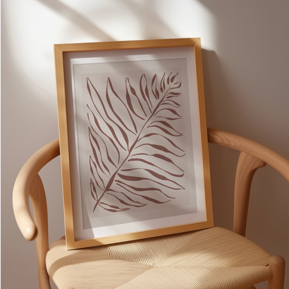 Akvarellposter med palmblad i terrakotta, inramad och placerad på flätad stol