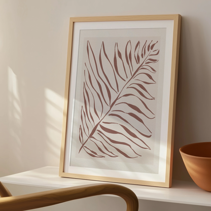 Akvarellposter med palmblad i terrakotta, inramad i ljust trä på konsolbord