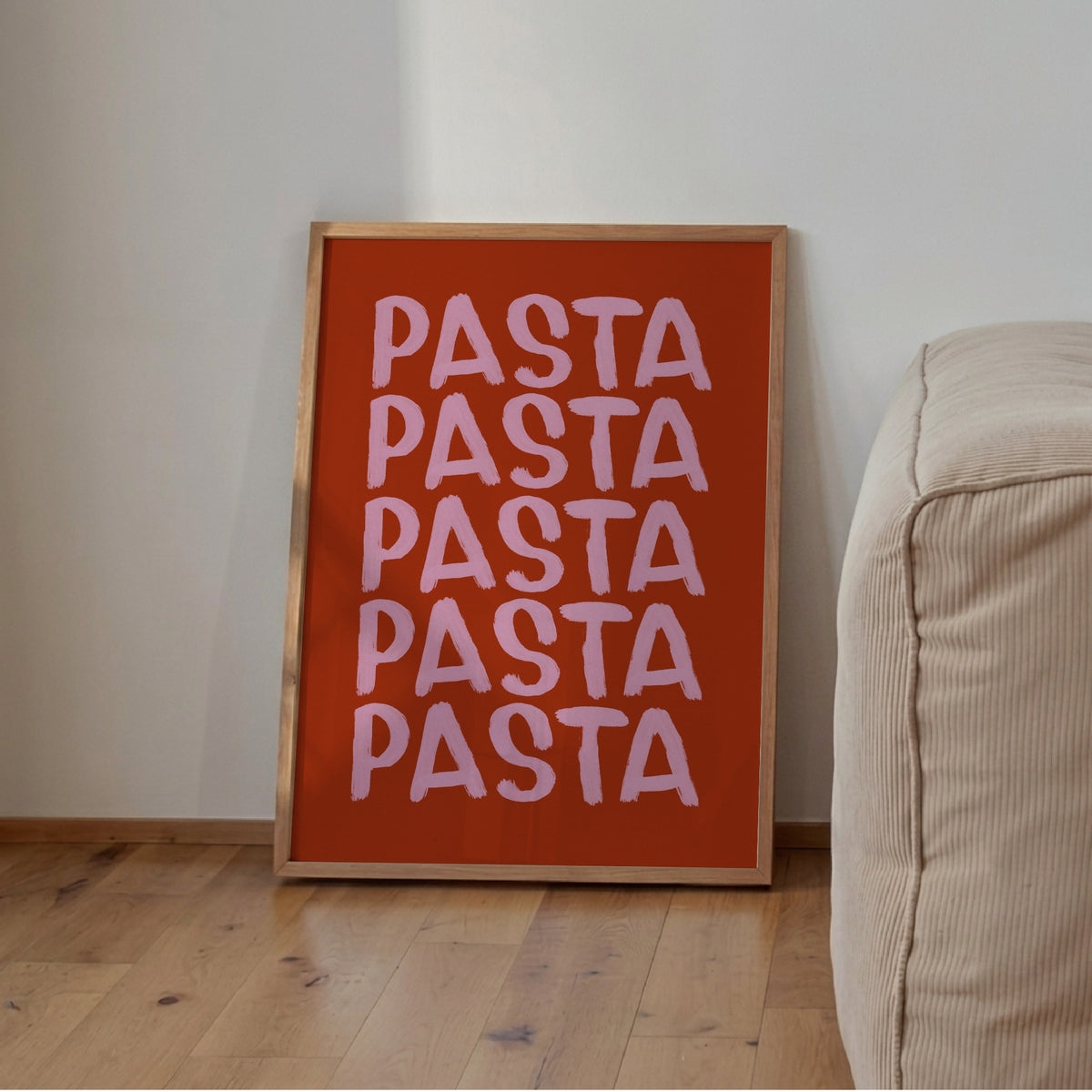 Pastaposter i rostrött och rosa lutad mot väggen bredvid en krämvit sittpuff