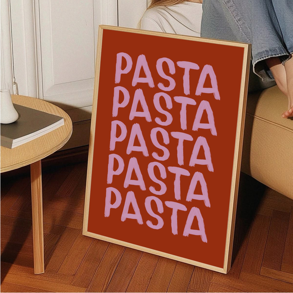 Pastaposter i träram lutad mot ett sidobord på fiskbensparkett