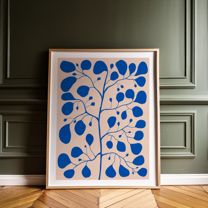 Blå botanisk poster med Pilea Peperomioides och vit kant, lutad mot en grön vägg i träram.