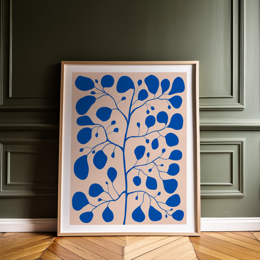 Blå botanisk poster med Pilea Peperomioides och vit kant, lutad mot en grön vägg i träram.