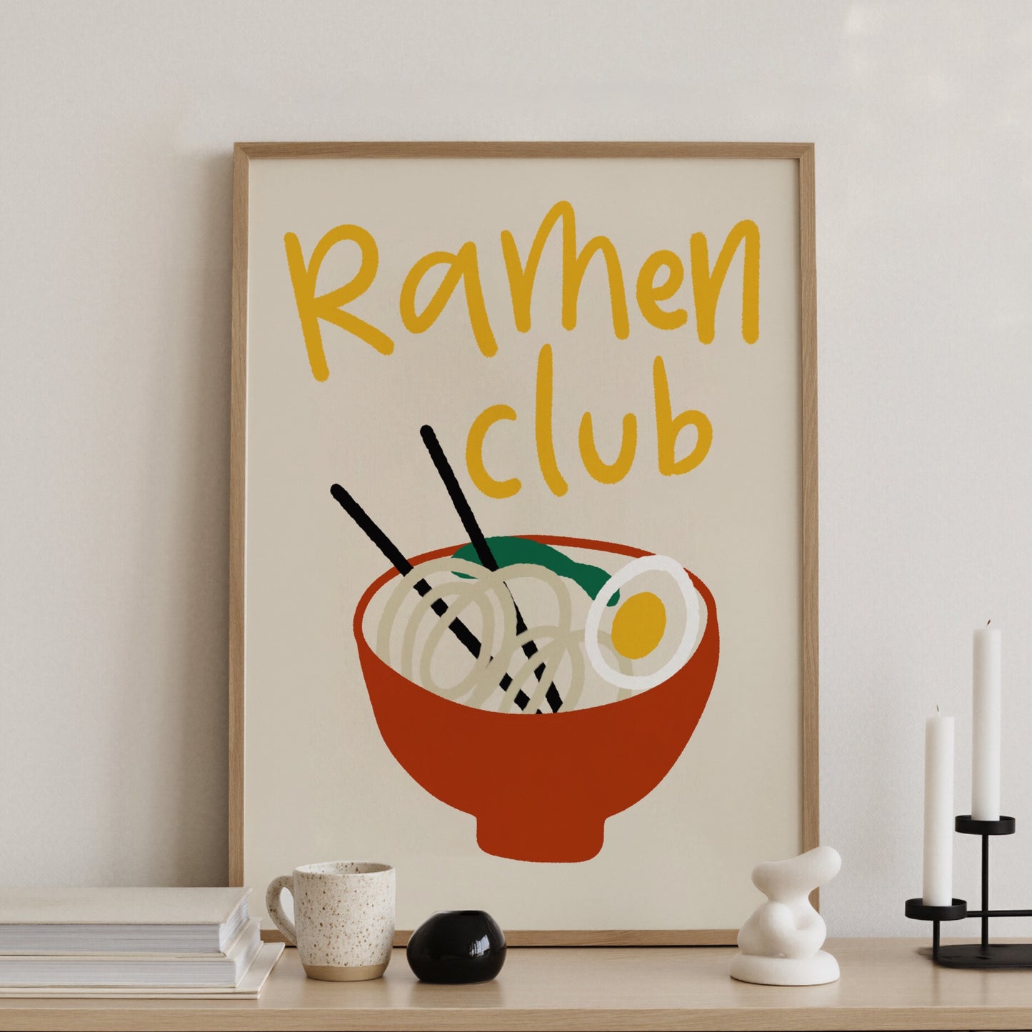 Ramenposter med handskriven text Ramen Club i gult, på konsolbord med ljusstakar