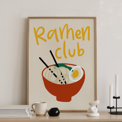 Ramenposter med handskriven text Ramen Club i gult, på konsolbord med ljusstakar
