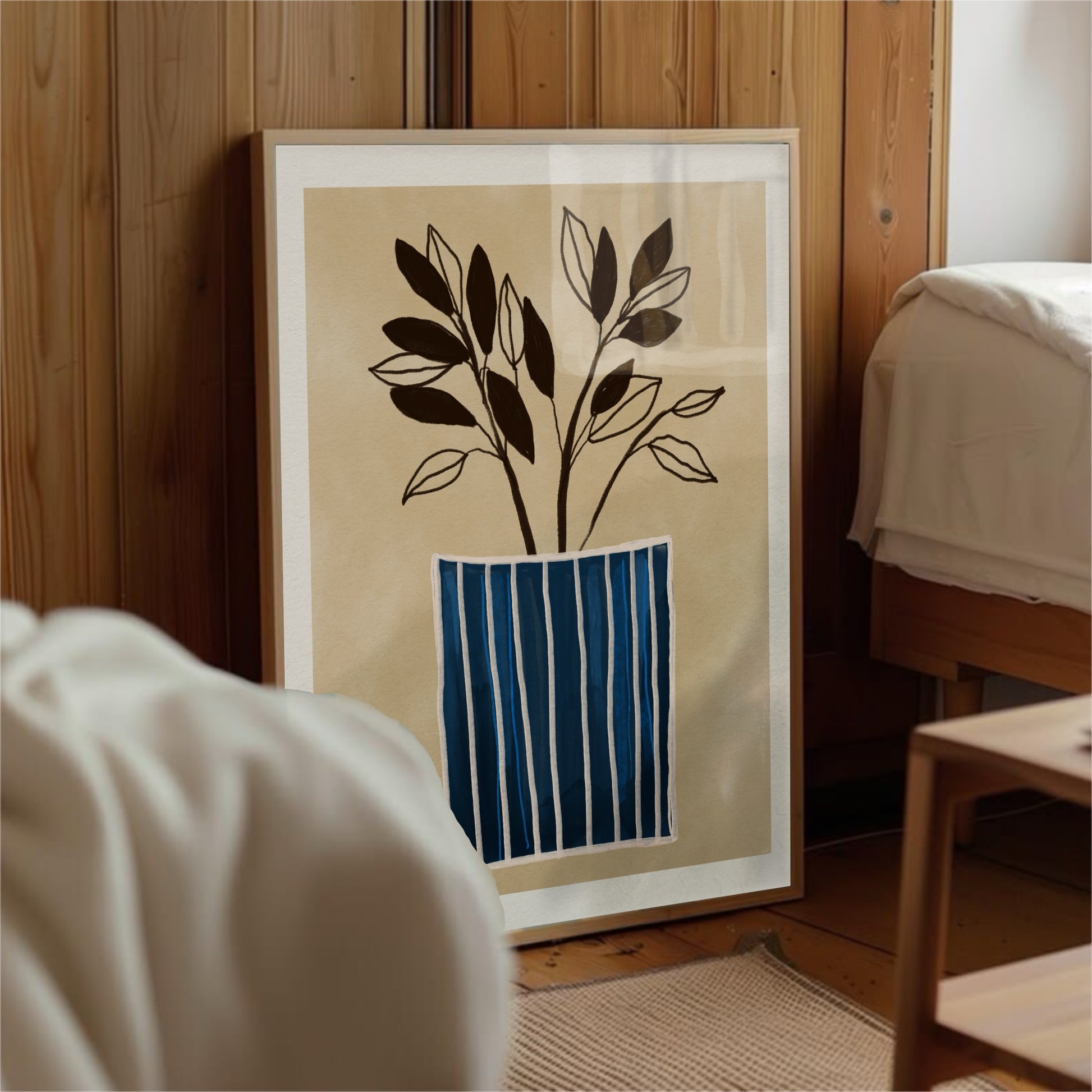 Minimalistisk botanisk poster med blårandig vas lutad mot en rustik trärpanelvägg på ett mörkt trägolv. Miljöbilden visar ett sovrum eller vardagsrum med en dagbädd i trä och linnekuddar, vilket skapar en ombonad och bohemisk atmosfär.
