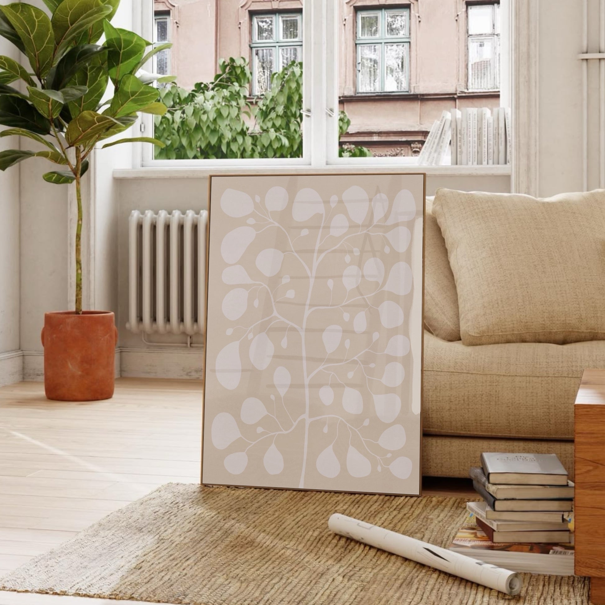 Inredningsdetalj med en stor Pilea-poster på varm beige canvas lutad mot en beige soffa, kombinerat med böcker och gröna växter för en naturnära stil.
