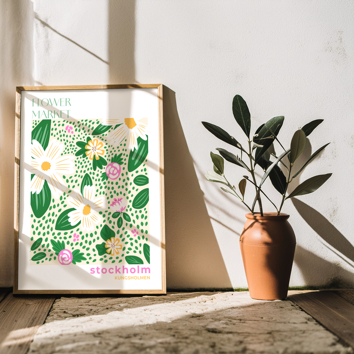 Flowermarket poster, blommor i klara färger tillsammans med texten Stockholm, Kungsholmen. Inramad i träram lutandes mot vit vägg i en rustik miljö med ljusinläpp