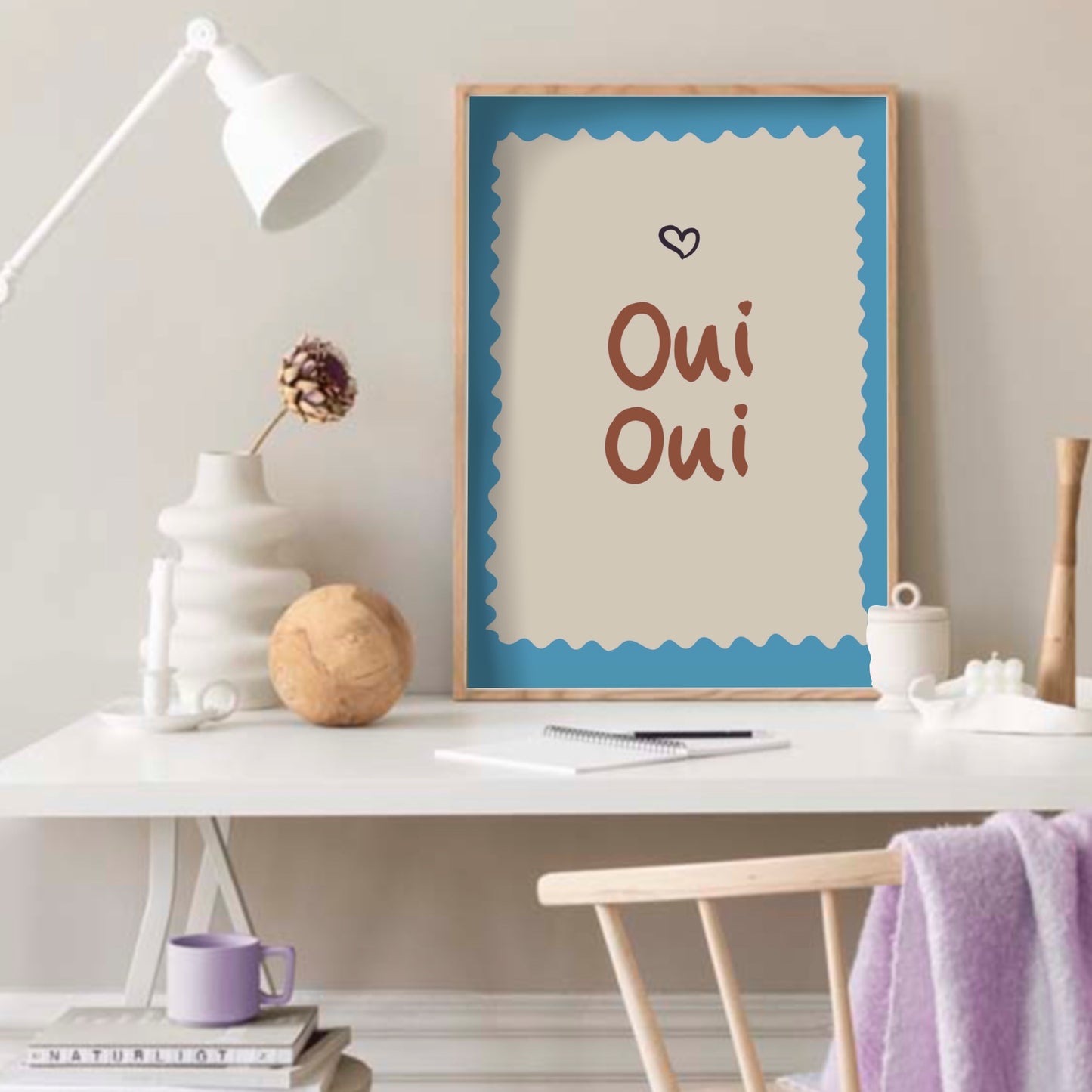 Inspiration för hemmakontor med en färgglad Oui Oui-poster på ett vitt skrivbord bredvid en lila kaffekopp.