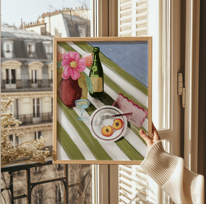 Livsstilsbild där en hand håller upp ett konsttryck framför ett fönster med utsikt över Paris takåsar. Motivet visar en somrig dukning med persikor och blommor.