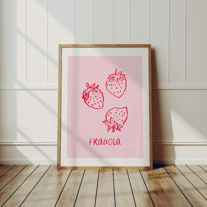 Fragola-postern i en ljus träram som lutar mot en vit panelvägg på ett ljust trägolv. En minimalistisk inredningsdetalj som visar hur postern fungerar som bohemisk väggdekor i ett vardagsrum.