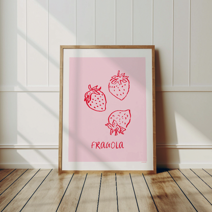 Fragola-postern i en ljus träram som lutar mot en vit panelvägg på ett ljust trägolv. En minimalistisk inredningsdetalj som visar hur postern fungerar som bohemisk väggdekor i ett vardagsrum.