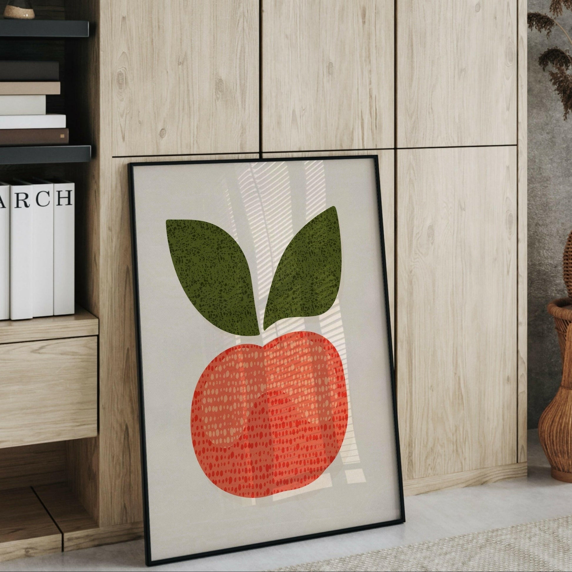 Äppel-postern i en svart ram som lutar mot en hylla med böcker