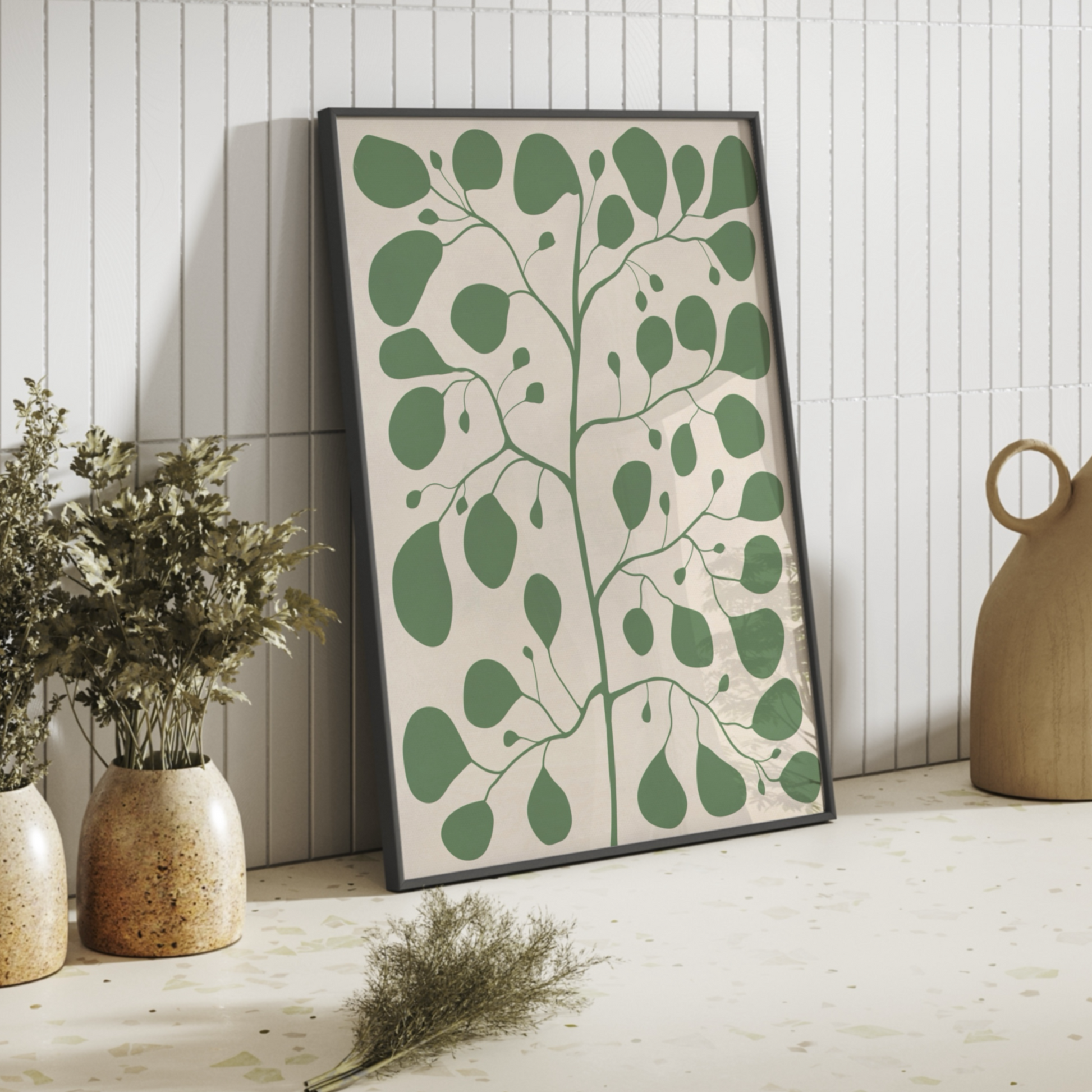 Stor Pilea-poster lutad mot en kaklad vägg i ett modernt badrum eller kök. Konstnärlig och organisk väggkonst i gröna toner kombinerat med keramikvaser.