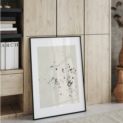 En inramad bläckstänk-poster som står lutad mot en trävägg i ett ljust rum. En stilren inredningsdetalj som representerar hållbar och modern stil.
