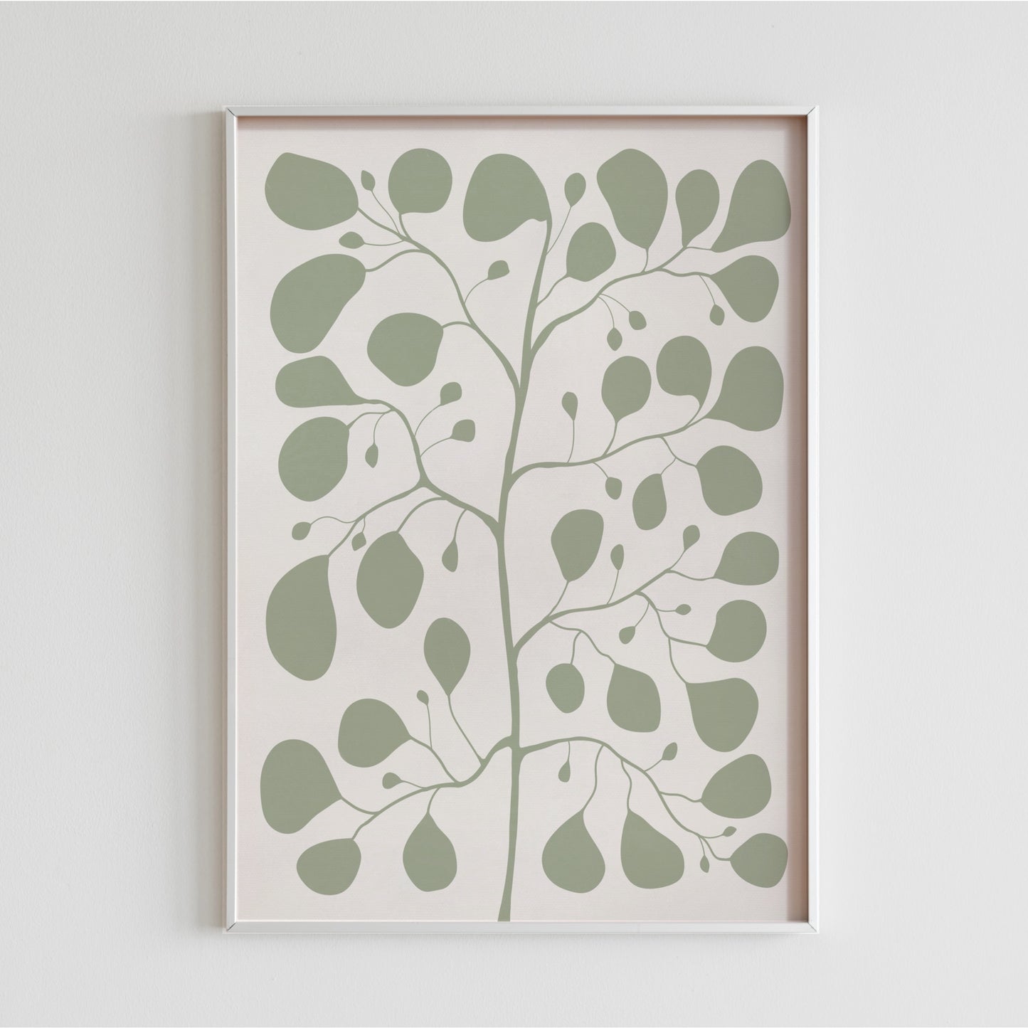 En vit ram med en jadegrön Pilea-illustration hängande på en ren, vit vägg som visar upp motivets minimalistiska och organiska former