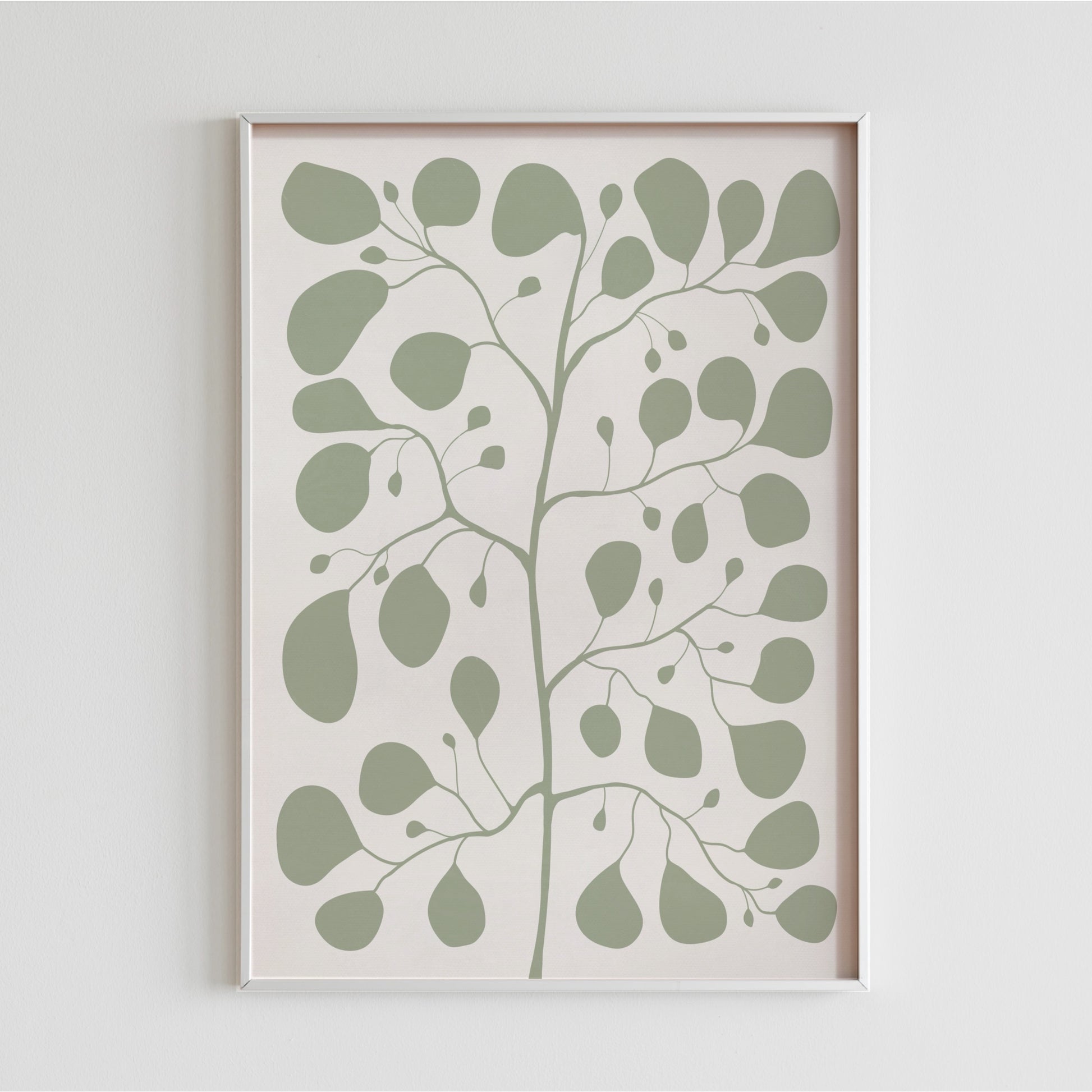 En vit ram med en jadegrön Pilea-illustration hängande på en ren, vit vägg som visar upp motivets minimalistiska och organiska former